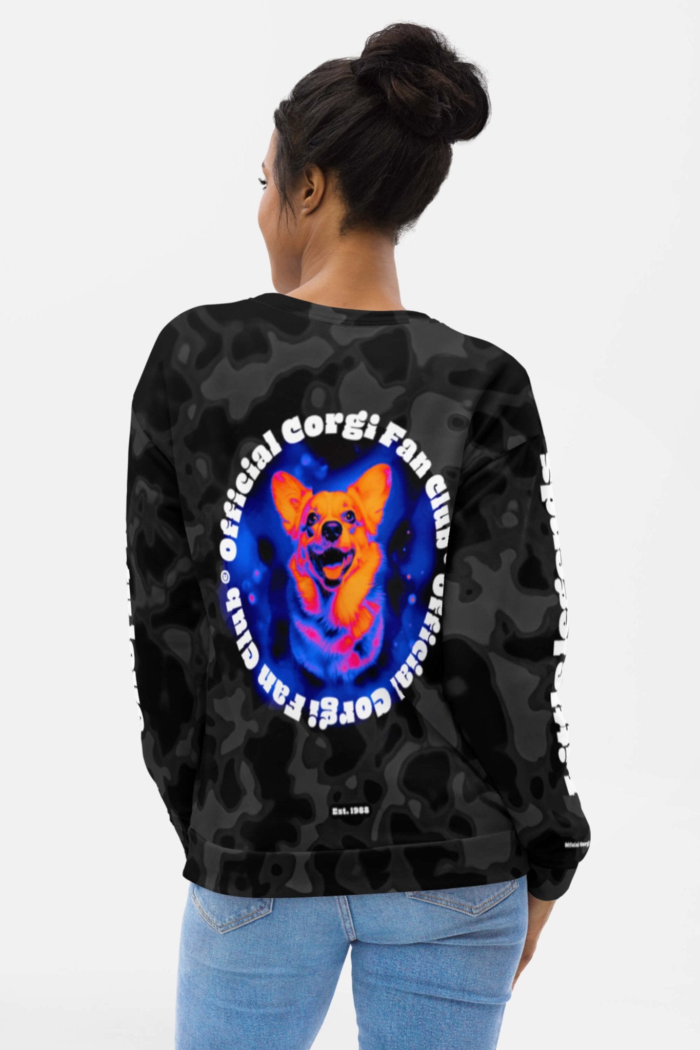 A woman with her hair in a bun wears the Dogloverclothing.com Official Corgi Fan Club© Elite Camo Sweatshirt—a black eco-friendly pullover with a smiling corgi and official corgi fan club text arranged in a circle.