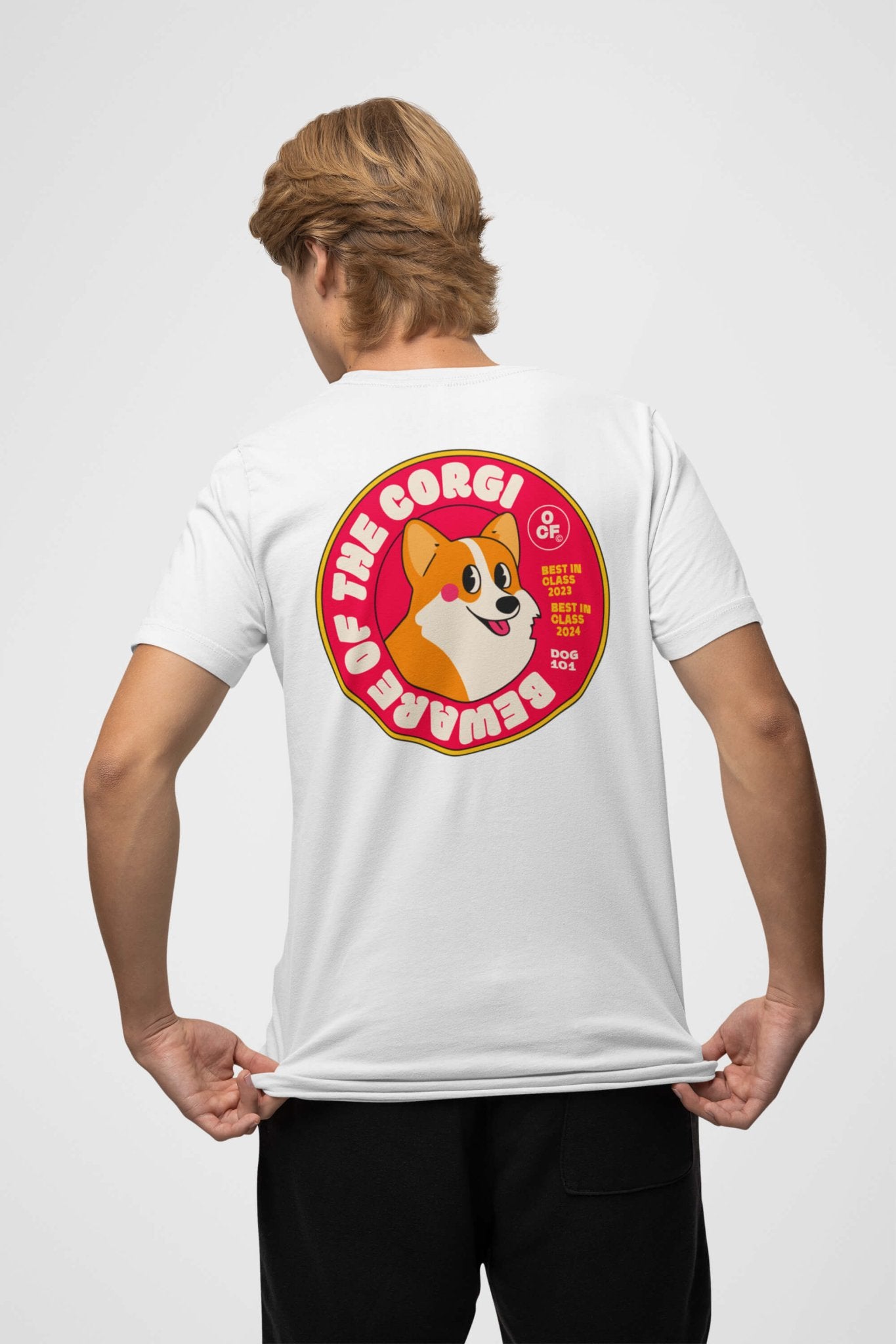 A person is wearing a Beware of the Corgi Supreme Unisex T-Shirt by Dogloverclothing.com. This white shirt, crafted from super comfy fabric, features a colorful cartoon corgi and The Corgi Brewer text on the back, with red and yellow accents. They face away, holding the hem.