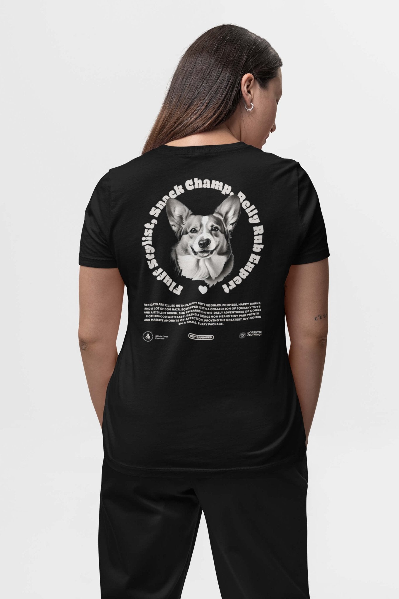 A person with long hair is facing away, wearing a Dogloverclothing.com black Corgi Mom Ultimate Tribute T-Shirt, featuring a smiling dogs face and text: Playful, Spunky, Stocky, Champion, Rally, Runner—ideal for dog lovers and proud Corgi Moms.