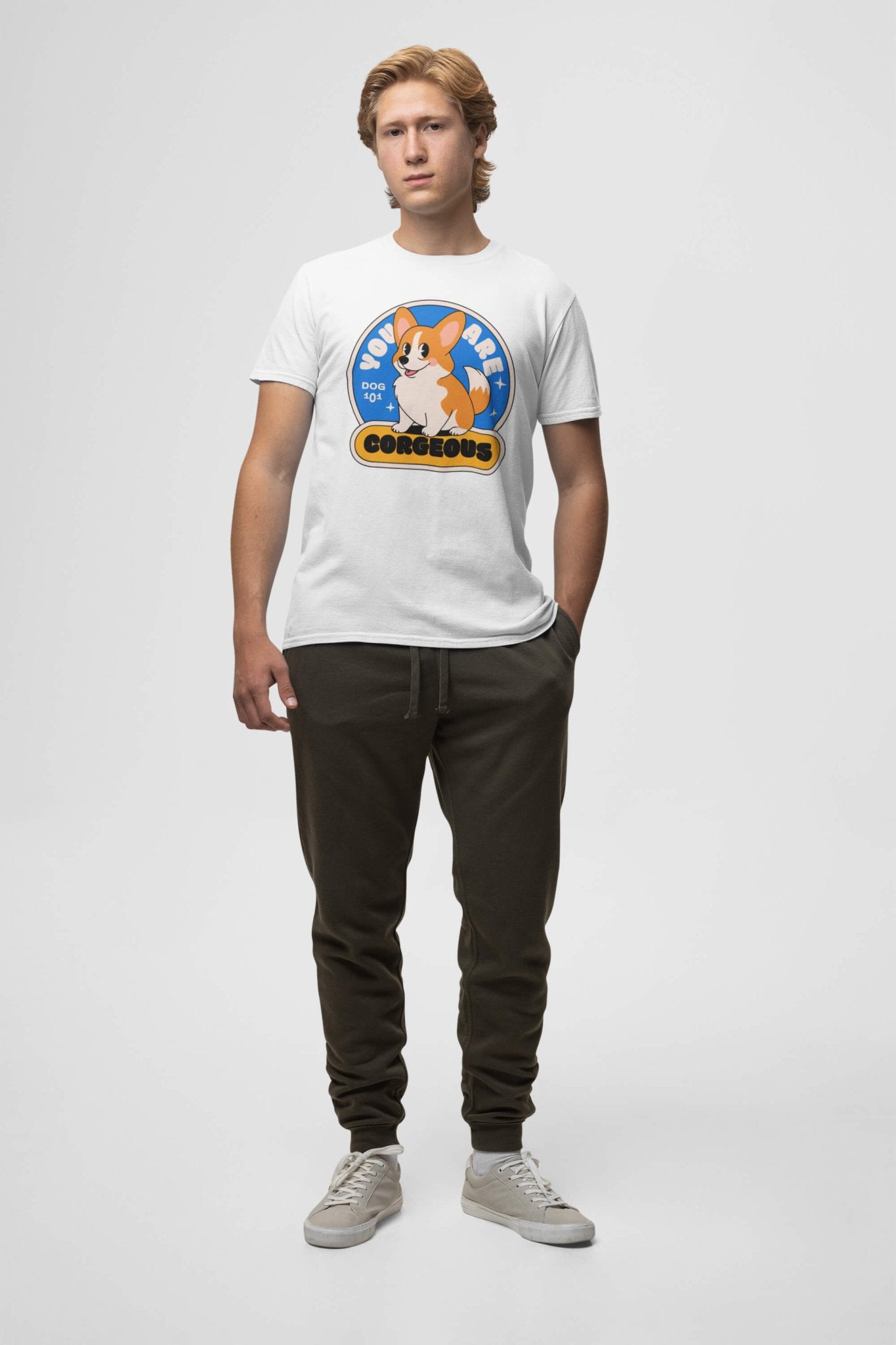 A light brown-haired person stands against a plain background wearing a Dogloverclothing.com premium cotton You are Corgeous Supreme T-Shirt with an illustrated fox. Their hands are in the pockets of their dark jogger pants and they wear white sneakers—a perfect outfit for dog lovers.