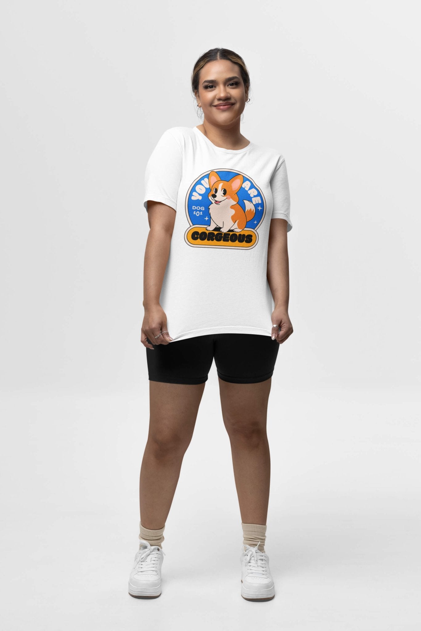 In a studio, someone wears the You are Corgeous Supreme T-Shirt from Dogloverclothing.com. It features a colorful cartoon corgi and Born To Be Corgelous. Ideal for dog lovers, theyre styled with black shorts, ankle socks, and sneakers against a plain white backdrop.