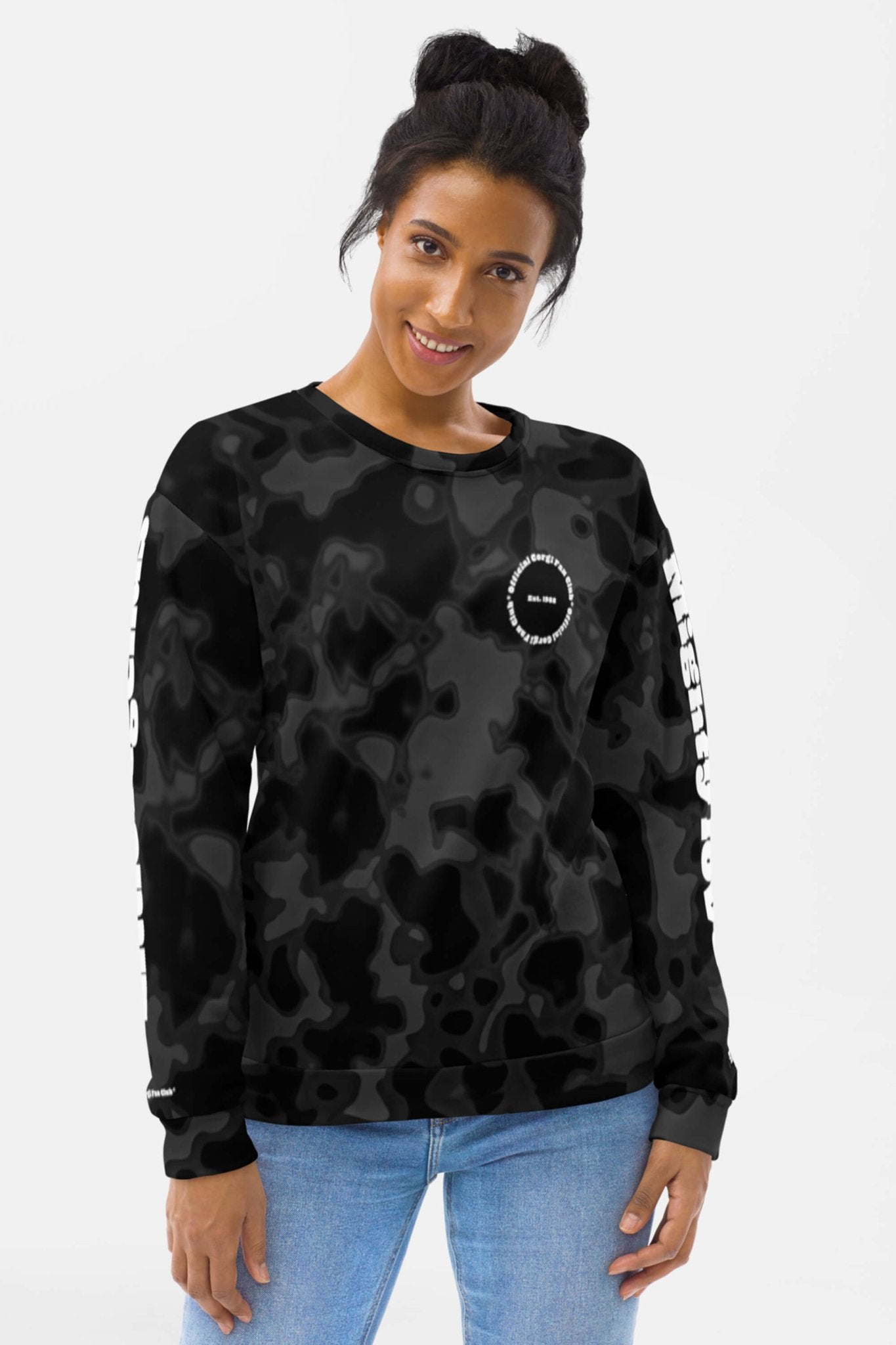 A woman with dark hair in a bun is wearing the Official Corgi Fan Club© Elite Camo Sweatshirt by Dogloverclothing.com, featuring white text on the sleeves and chest, smiling against a plain white background.