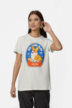 A woman with long brown hair and large hoop earrings is wearing a light gray Best Dog Supreme Tribute Unisex T-Shirt from Dogloverclothing.com, featuring a colorful corgi graphic and the text Sit-Stay-Play, Best Dog—perfect for dog lovers. She touches her ear with one hand.