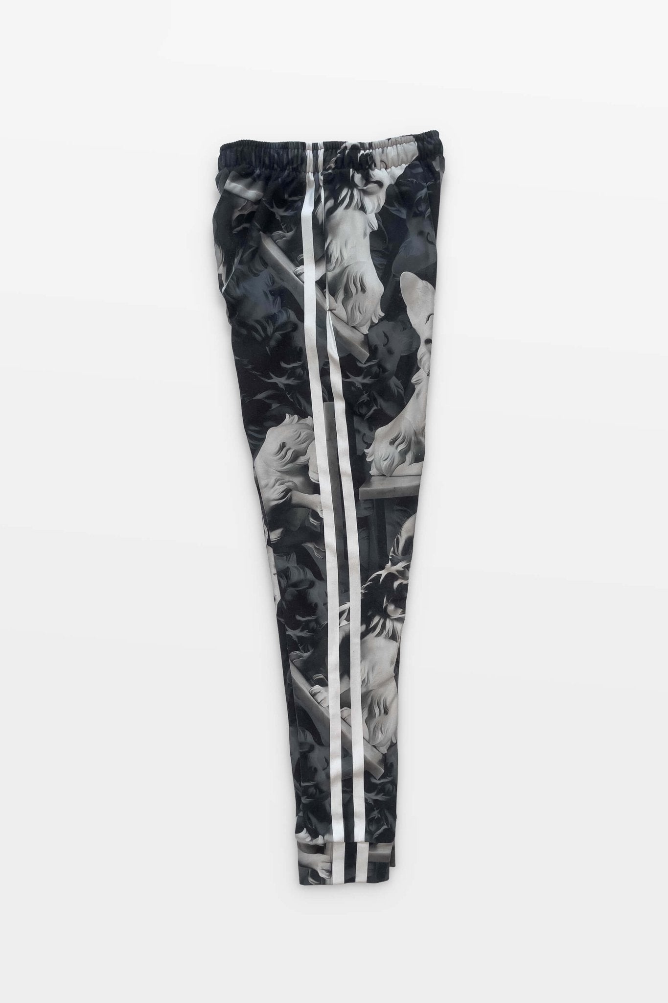 Corgi Supreme Tribute Joggers by Dogloverclothing.com are black and white athleisure pants with a camo-style print featuring artistic statue imagery. Made from recycled materials, they have two white stripes down the sides and are set against a plain white background.