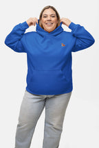 A person smiles while adjusting the hood of a bright blue Classic Corgi Sidekick Embroidered Unisex Hoodie from Dogloverclothing.com, featuring a butterfly patch on the chest. Paired with light gray jeans for maximum comfort, all set against a plain white background.