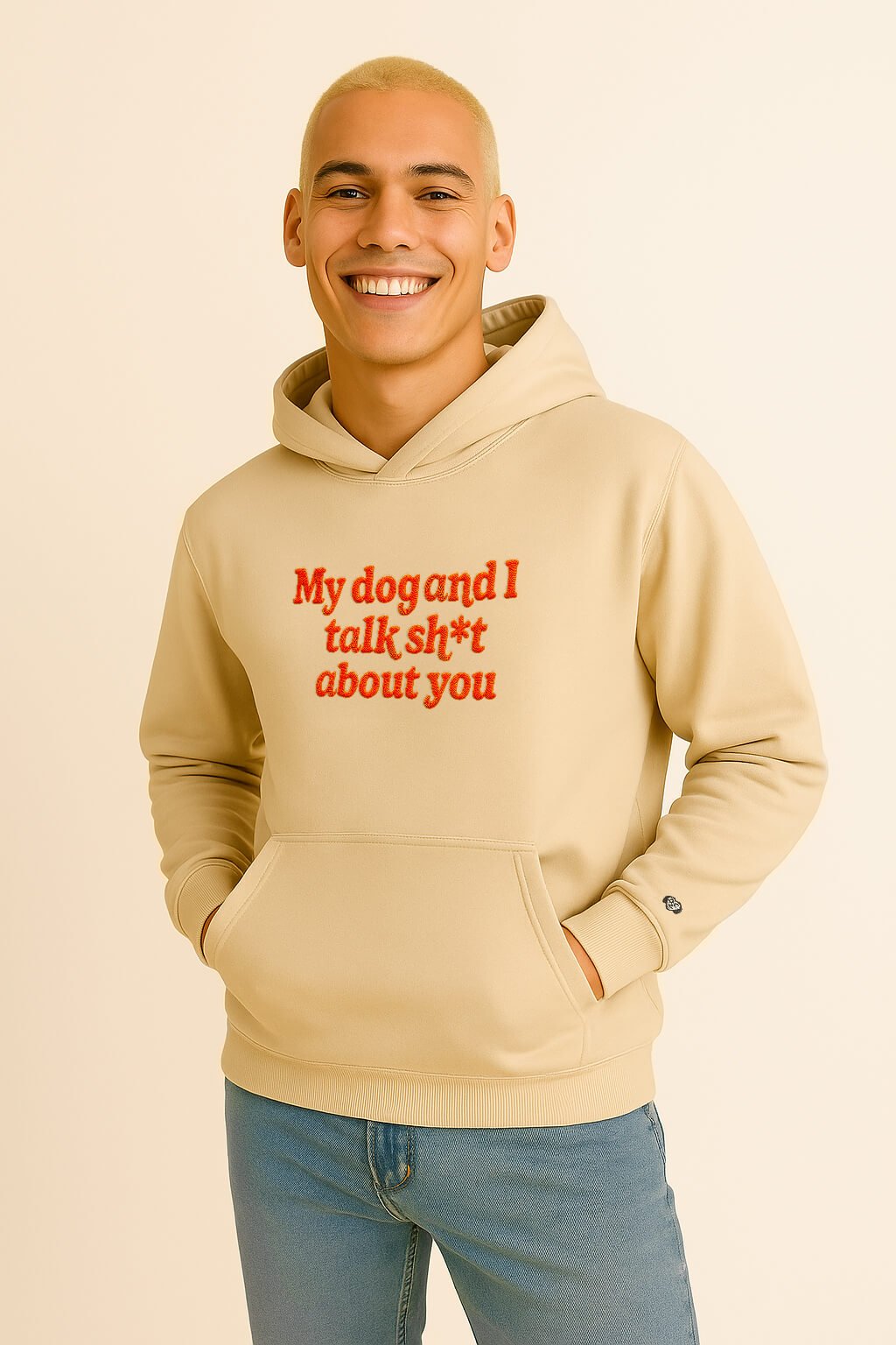 A smiling model wears the Bold My Dog And I Talk Embroidered Hoodie by Dogloverclothing.com—a premium beige hoodie with red text, posing with one hand in the pocket against a light background for comfort.