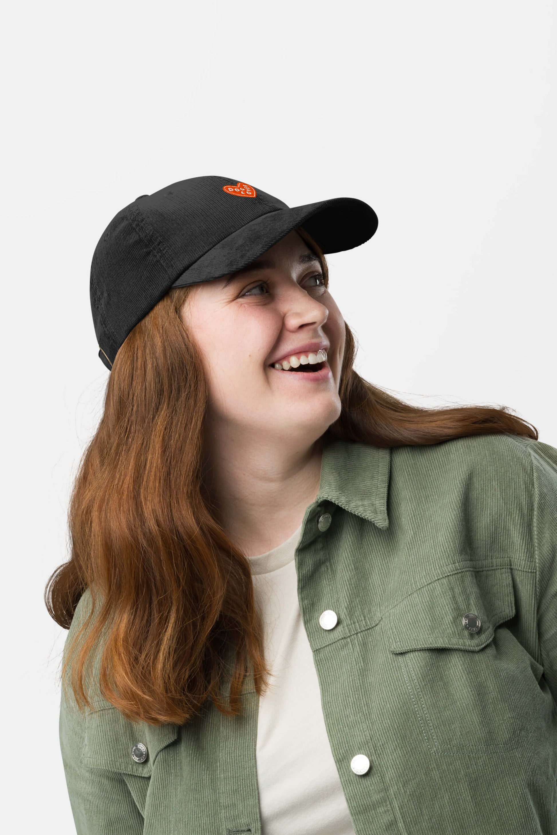 A smiling person with long brown hair wears the Limited Dog Lover Corduroy Cap from Dogloverclothing.com, styled with a light green button-up shirt and white T-shirt, looking up against a plain white background.