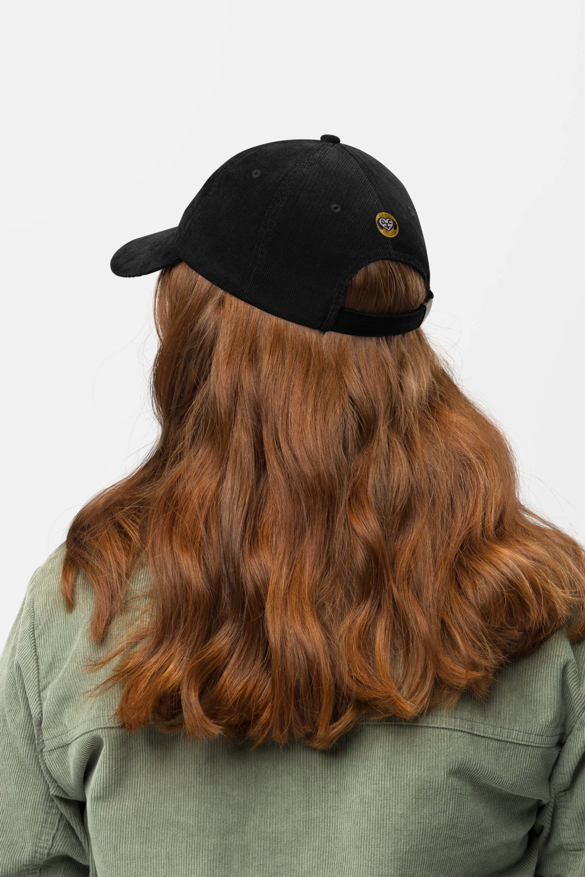 A person with long, wavy auburn hair wears the Limited Dog Lover Corduroy Cap from Dogloverclothing.com and a green textured shirt, facing away from the camera against a plain white background.