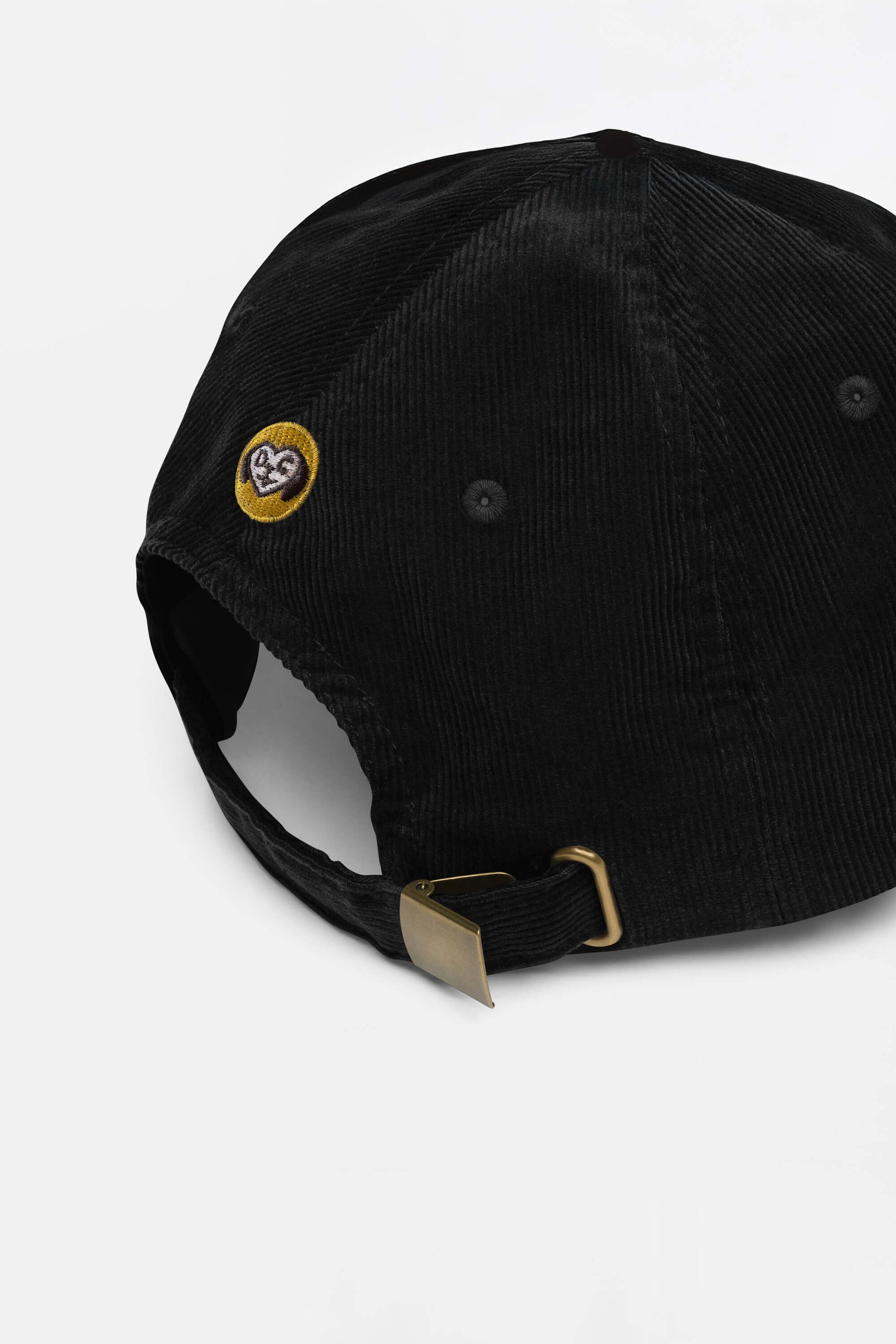 The Limited Dog Lover Corduroy Cap from Dogloverclothing.com features a brass buckle strap and a small yellow embroidered smiling heart patch, showcasing its adjustable fit and dog lover charm.