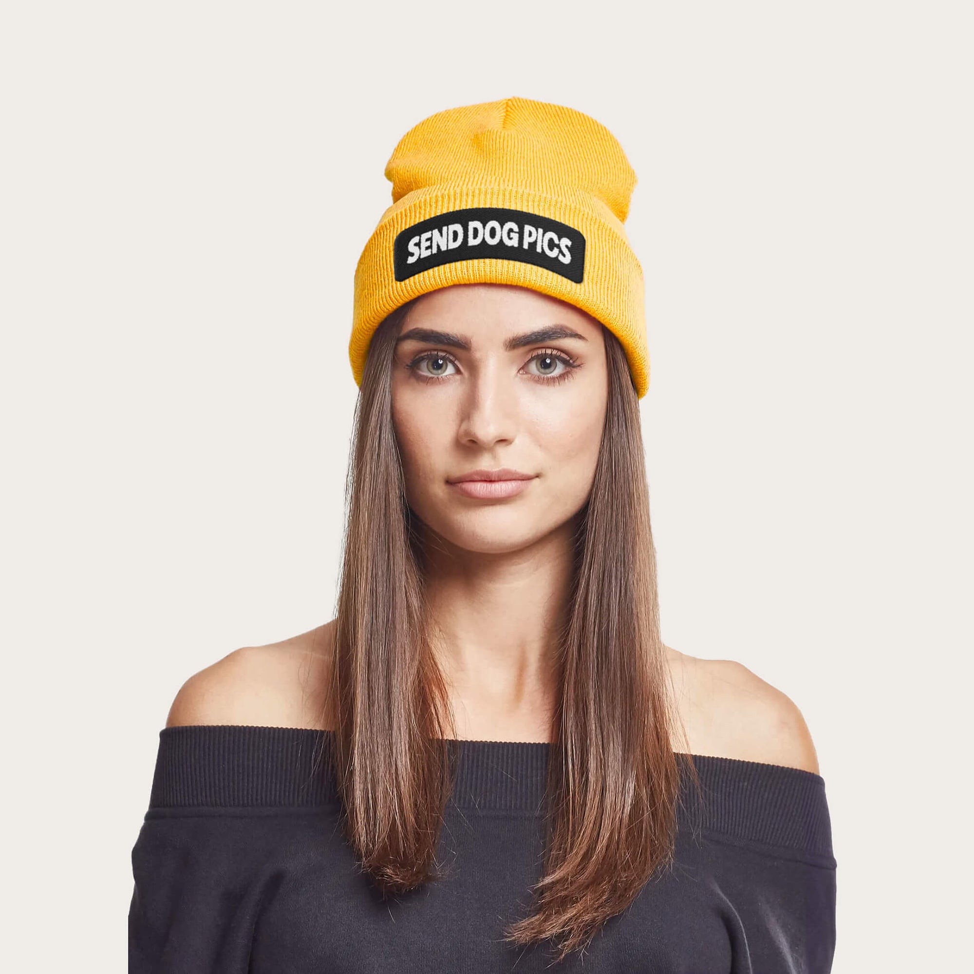 A long-haired person wears a Dogloverclothing.com Send Dog Pics bright yellow beanie, paired with an off-the-shoulder black top, against an off-white background, showcasing style and canine devotion in this dog lover apparel.