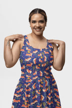 A woman joyfully poses with her hands near her shoulders, wearing a sleeveless dress adorned with colorful foxes and leaves on white. Her forearm reveals a small tattoo, capturing the vibrant whimsy of Dogloverclothing.coms Cute Corgi Garden Party Skater Dress.