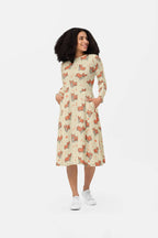 A woman beams in the Cozy Corgi Long Sleeve Midi Dress from Dogloverclothing.com, perfectly blending comfort and style. With curly hair and white sneakers, she exudes a relaxed vibe, hands tucked into the dress pockets against a plain white backdrop.