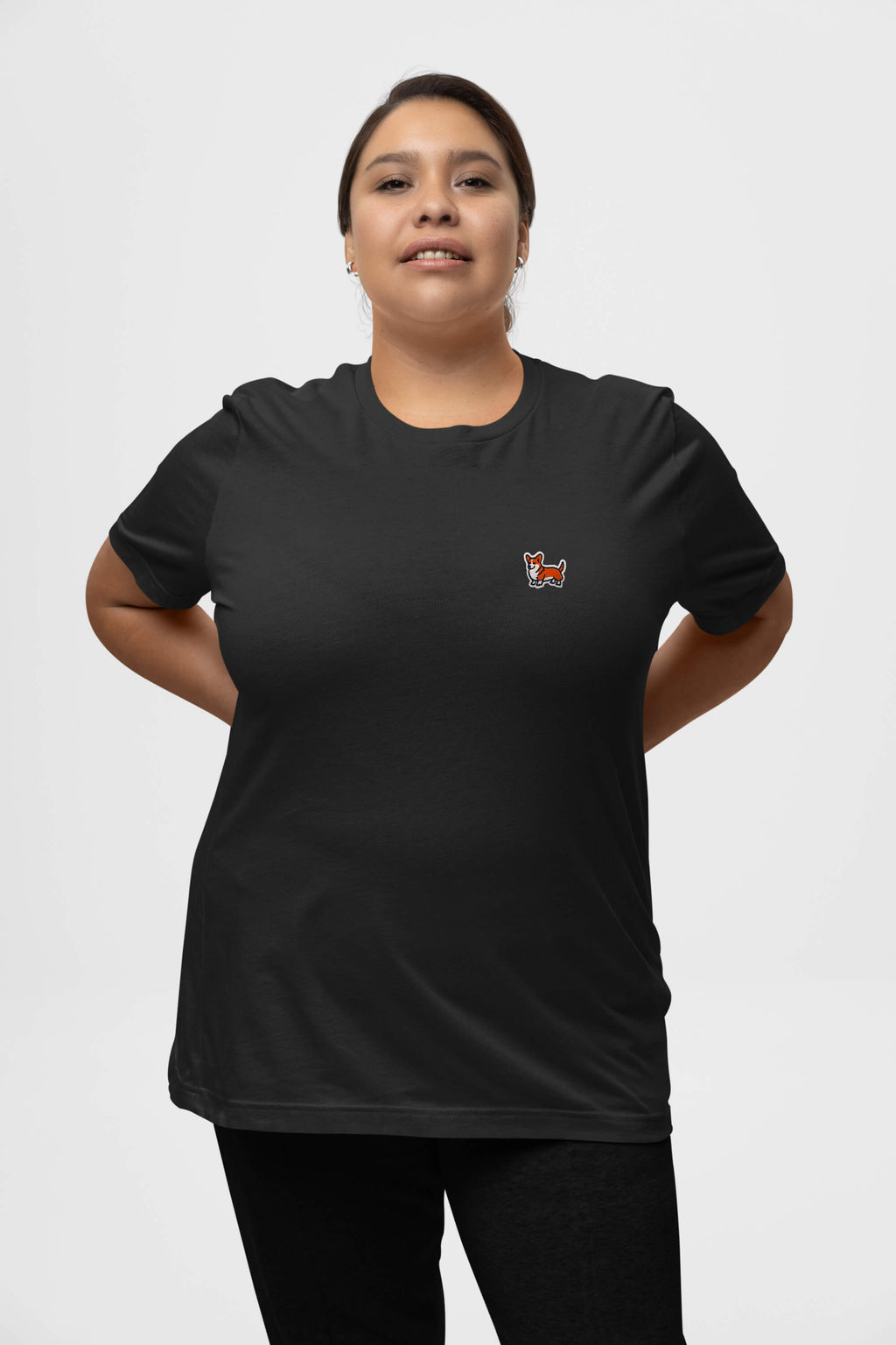 Wearing a Corgi Tail Wagger Unisex T-Shirt from Dogloverclothing.com, someone stands confidently with hands behind their back. The shirts colorful design, reminiscent of a foxs head on a plain white background, perfectly embodies the spirit of Corgi enthusiasts.