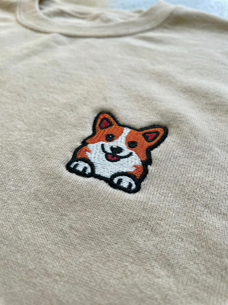 Close up of the corgi embroidery on the beige sweatshirt from WOOF