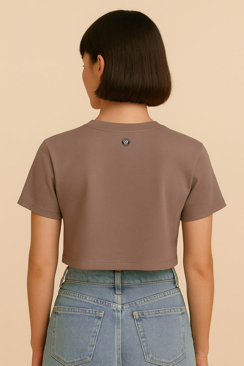 A person with short brown hair is shown from the back wearing the Oversized Dog Mom Crop Top by Dogloverclothing.com and high-waisted light blue jeans against a beige background, capturing an effortless Dog Mom Lifestyle vibe.
