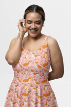 A person with a wrist tattoo smiles in an Adorable Corgi Summer Dress by Dogloverclothing.com, gently touching their hair and closing their eyes against a plain white studio backdrop.