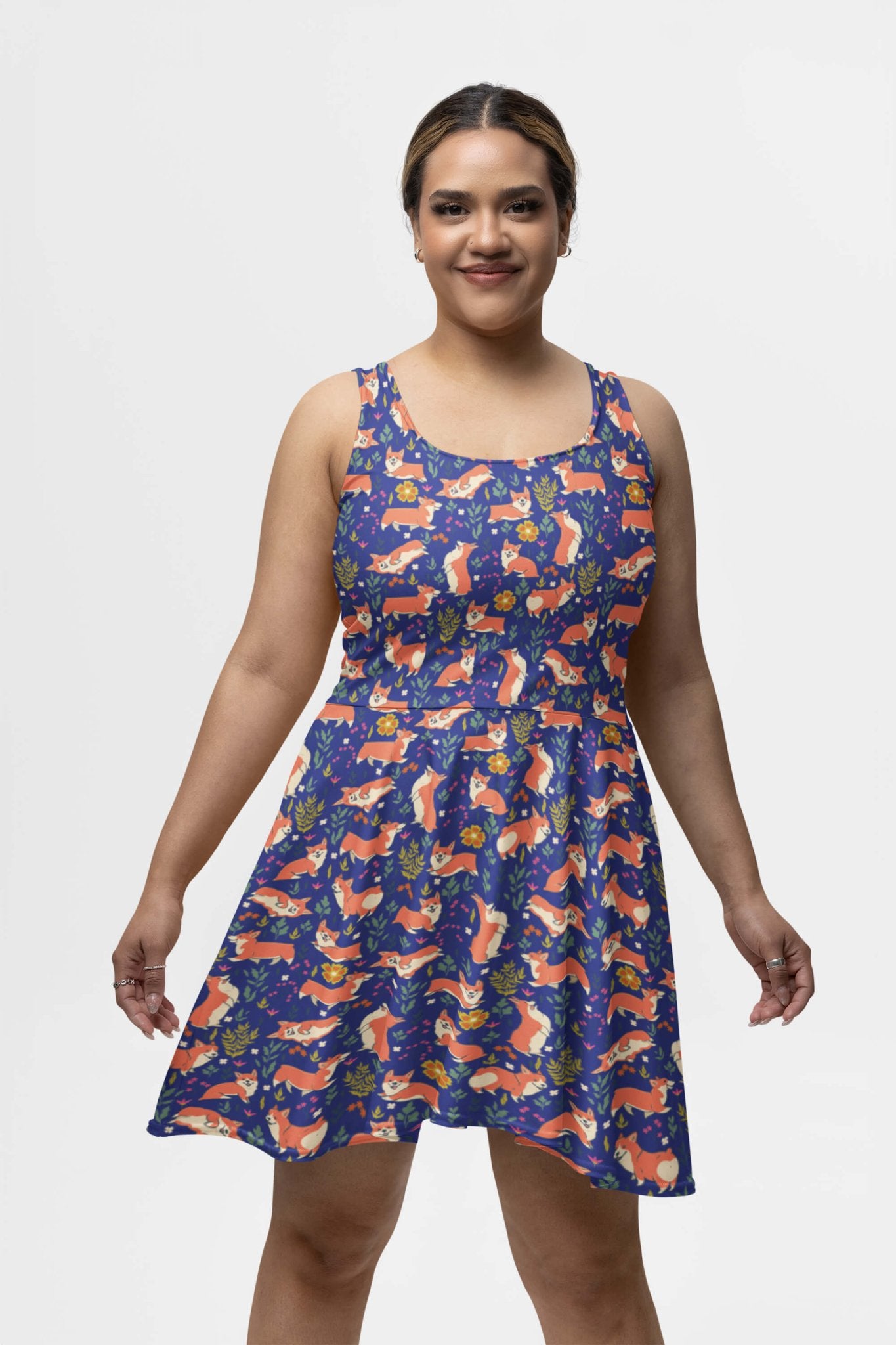 Against a white background, a person smiles with hands relaxed at their sides while wearing the Cute Corgi Garden Party Skater Dress from Dogloverclothing.com, featuring sleeveless design and colorful abstract patterns in red, orange, and blue.