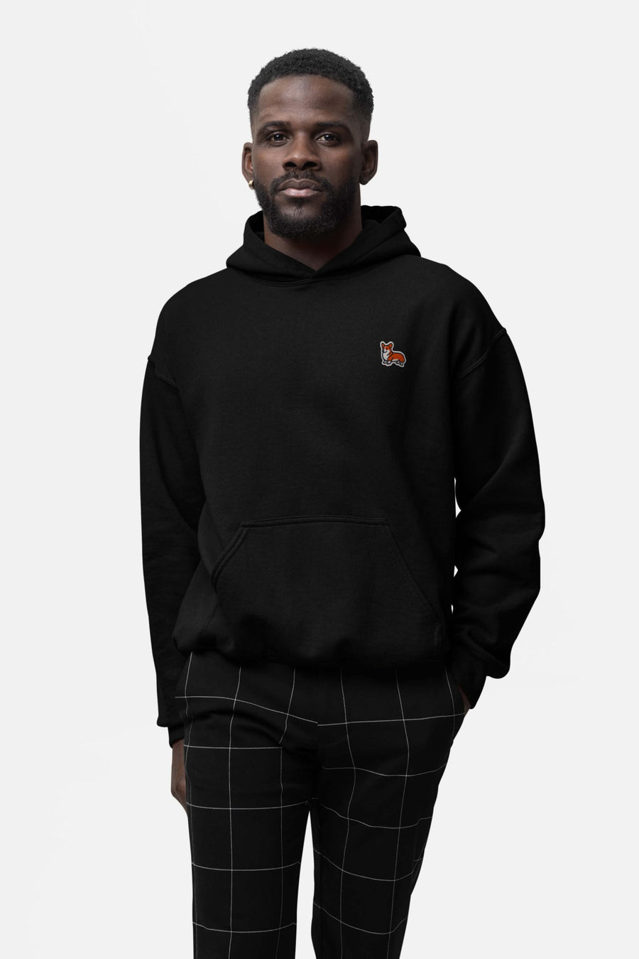 Man in the black Classic Corgi Sidekick Embroidered Hoodie from WOOF with plaid trousers