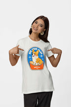 A smiling woman with long brown hair and hoop earrings points at her Best Dog Supreme Tribute Unisex T-Shirt by Dogloverclothing.com, made from premium cotton. It features a cute cartoon Corgi on a cushion within a badge design with the text, Sit. Stay. Slay. Perfect for dog lovers!.