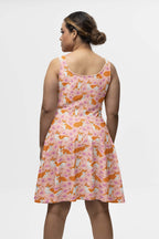 A person with brown hair is wearing the Adorable Corgi Summer Dress by Dogloverclothing.com, featuring a vibrant pink design with orange foxes and white stars. Against a plain white background, they face away from the camera, exuding playful charm and corgi cuteness.