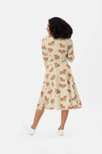 A woman with curly hair dons the cream-colored Cozy Corgi Long Sleeve Midi Dress from Dogloverclothing.com, showcasing the playful Corgis Everywhere pattern. Paired with white sneakers, she effortlessly embodies comfort and style against a plain white backdrop.