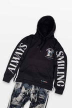 The Corgi Supreme Tribute Hoodie from Dogloverclothing.com is black with ALWAYS SMILING on the sleeves and a face graphic with colorful elements. It pairs with gray camo pants featuring Always Smiling on the left leg, made from eco-friendly, recycled materials and accented by colorful mini flags near the bottom.