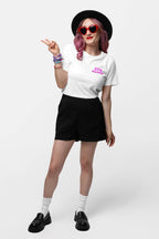 A pink-haired woman poses against a white backdrop wearing red heart-shaped sunglasses, a black hat, black shorts, loafers with white socks, and an ultra-soft Dog Mama Balloon T-Shirt featuring Doja Hasha text from Dogloverclothing.com while flashing a peace sign and embracing her pup-inspired style.