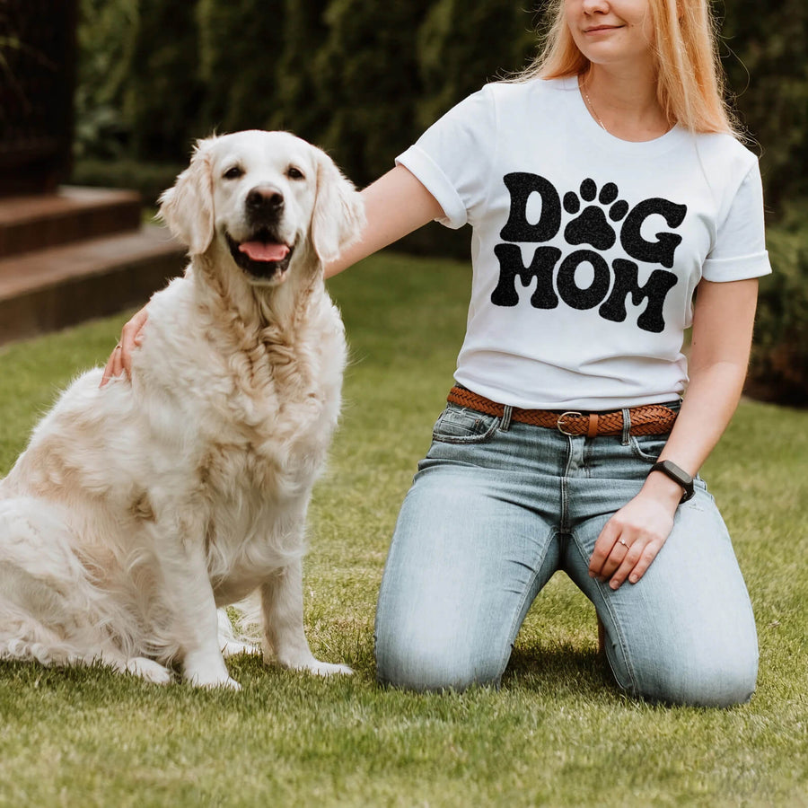Woman in the white Dog Mom T-Shirt from WOOF kneeling on grass next to her Golden Retriever in a bandana