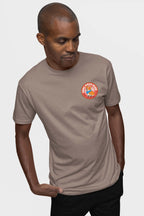 A man confidently dons a taupe Cool Dogs Club Unisex Hype T-Shirt from Dogloverclothing.com. With short hair and hands tucked in black pants pockets against a white background, he embodies the perfect style for dog enthusiasts.