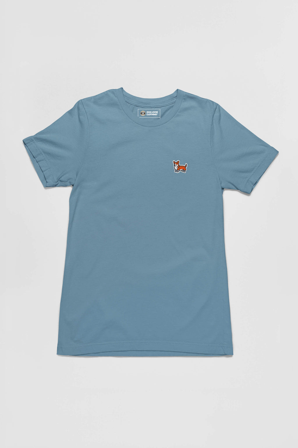 The Corgi Tail Wagger Unisex T-Shirt from Dogloverclothing.com is a light blue, short-sleeve tee featuring an embroidered long-tailed corgi patch on the left chest. Laid flat on a white background, this shirt is perfect for corgi enthusiasts who adore their fluffy friends.
