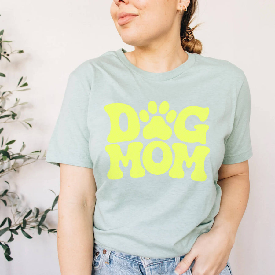 Person in the light green Dog Mom T-Shirt from WOOF with bold yellow DOG MOM lettering and a paw print