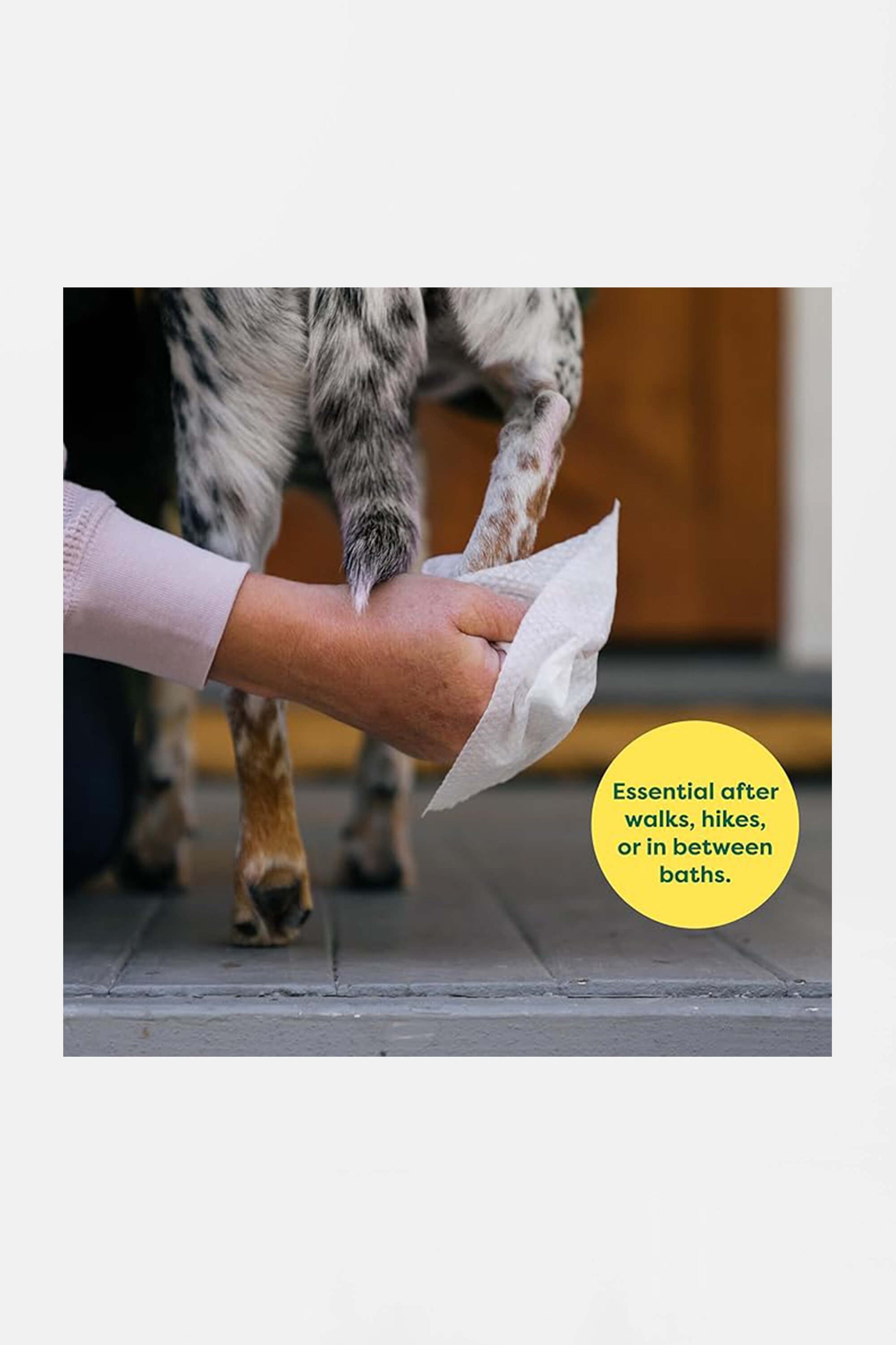 A person wipes a dogs muddy paw with an Amazon Hypoallergenic Earth Rated Pet Wipe. A yellow circle reads, Essential after walks, hikes, or in between baths. The background features a partially visible door.