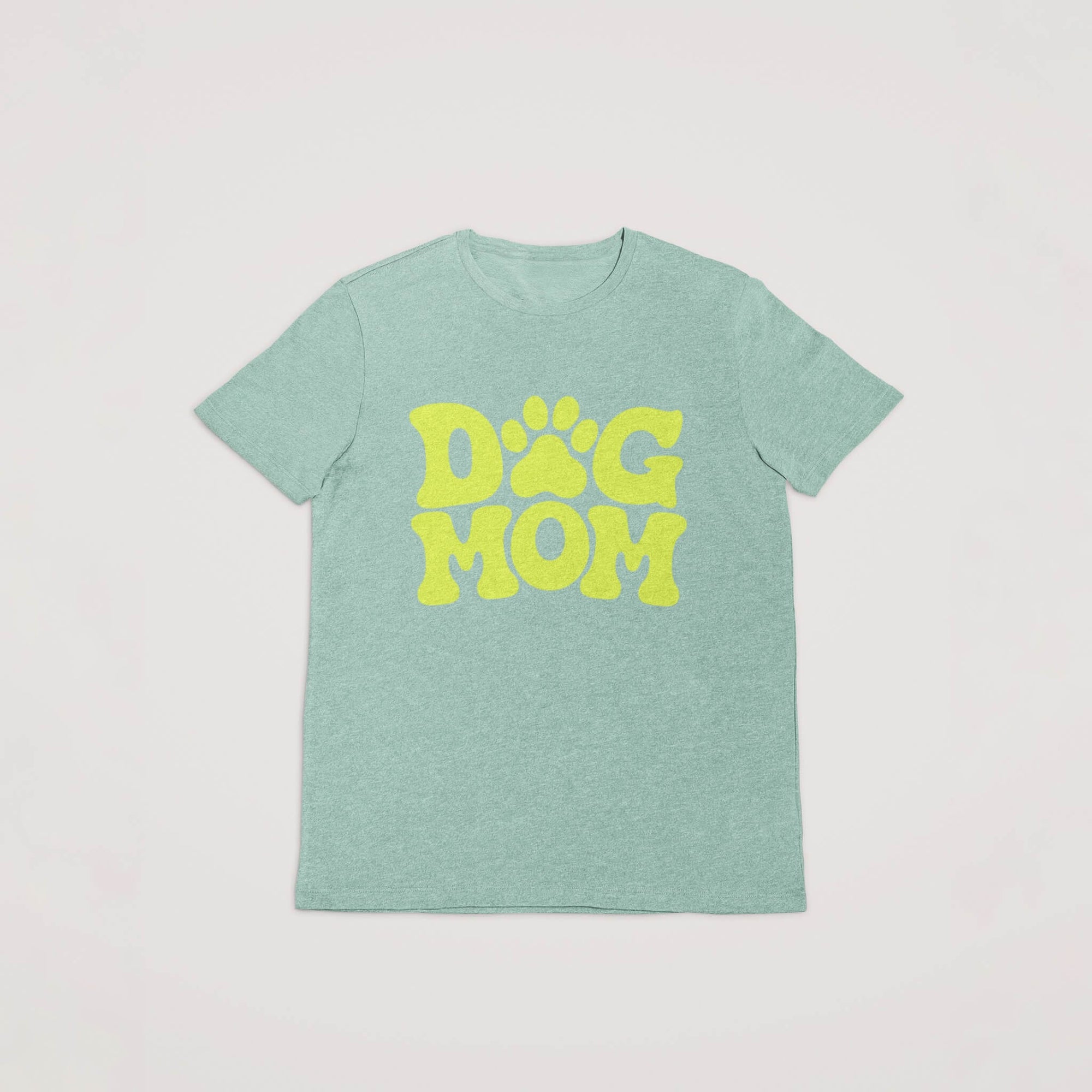Dogloverclothing.coms light green Dog Mom T-Shirt features bold yellow DOG MOM text with the O formed as a paw print, perfect for dog lovers. Laid flat on a white background, it stands out among dog lover items.