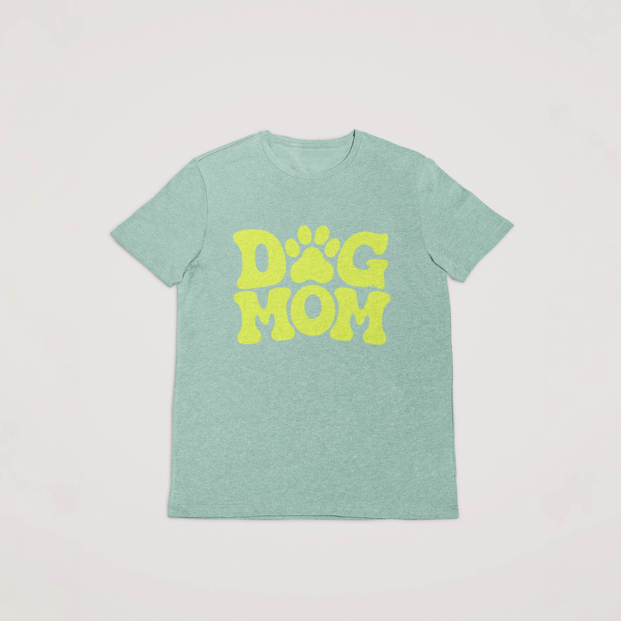 Dogloverclothing.coms light green Dog Mom T-Shirt features bold yellow DOG MOM text with the O formed as a paw print, perfect for dog lovers. Laid flat on a white background, it stands out among dog lover items.