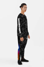 A person stands sideways in Dogloverclothing.coms Official Corgi Fan Club© Elite Camo Joggers, featuring colorful stripes and a comfy fit, paired with black sneakers against a plain white background.