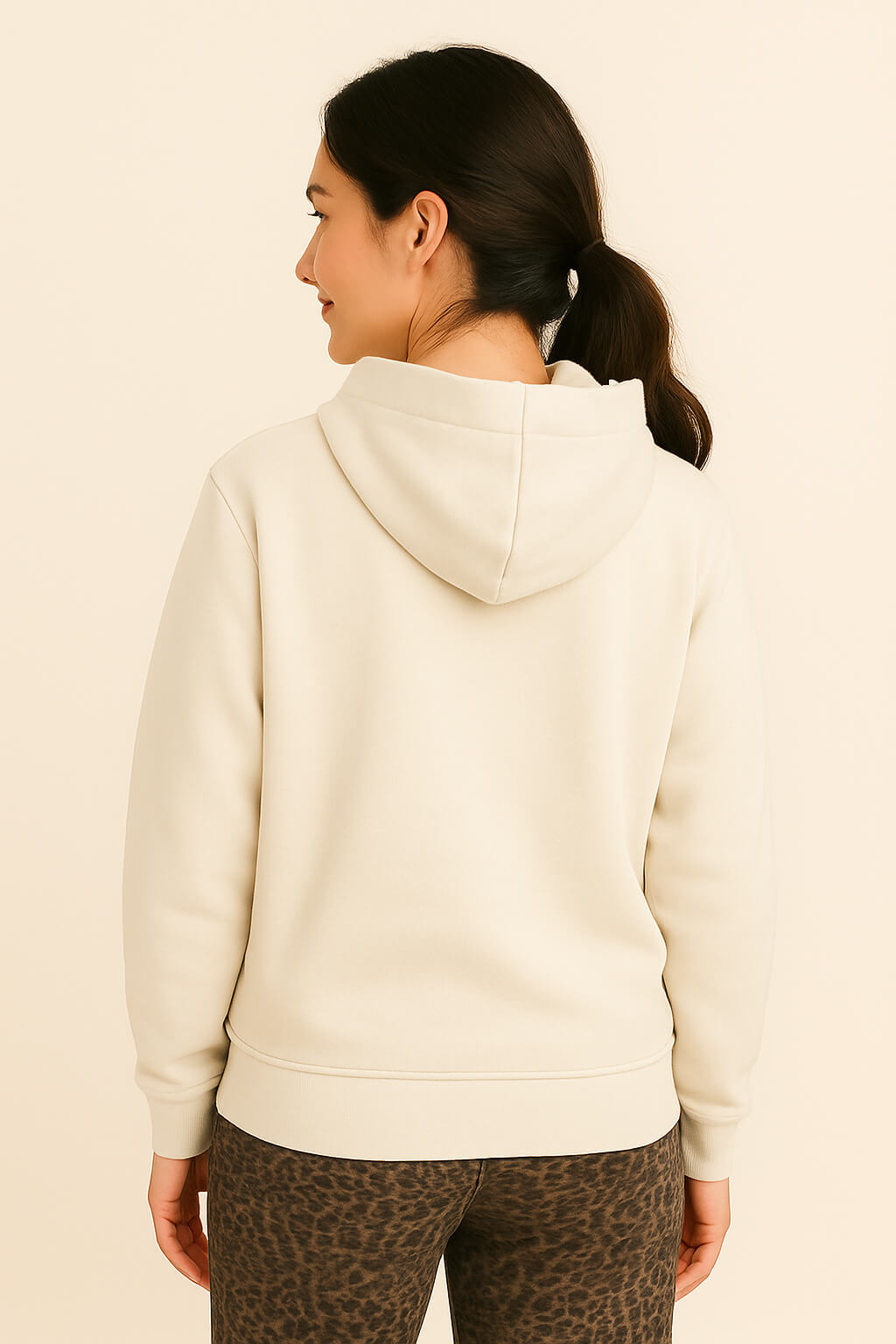 A woman with dark hair in a ponytail wears the Super Soft Dog Love Hoodie by Dogloverclothing.com, showing an embroidered LOVE design, with animal print leggings, standing with her back to the camera against a plain light background.