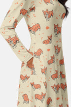 A person wears the Cozy Corgi Long Sleeve Midi Dress from Dogloverclothing.com, featuring playful corgis and orange splatters on beige. The fitted waist elegantly flares, with a hand tucked in a pocket—where comfort meets style effortlessly.