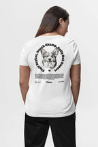 A person with long hair, in a white Dogloverclothing.com t-shirt and black pants, faces away from the camera. The Corgi Mom Ultimate Tribute T-Shirt features a circular design of a smiling dog with Snack Champ, Party Pup, and Playful Spirit—ideal for dog lovers or any Corgi Mom.