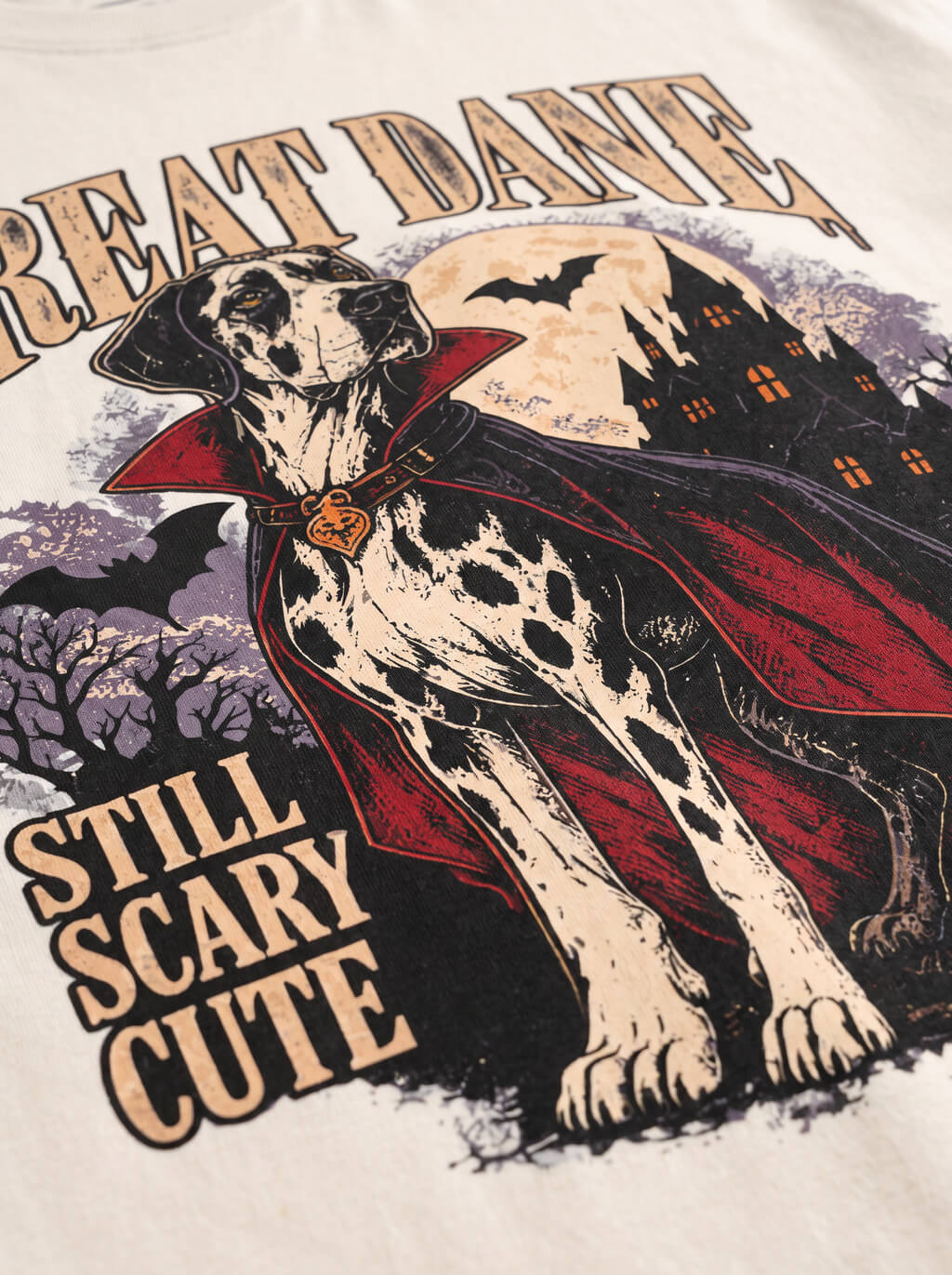 Close-up of the "Great Dane – Still Scary Cute" print with a Harlequin Great Dane in a vampire cape on the Vintage White tee
