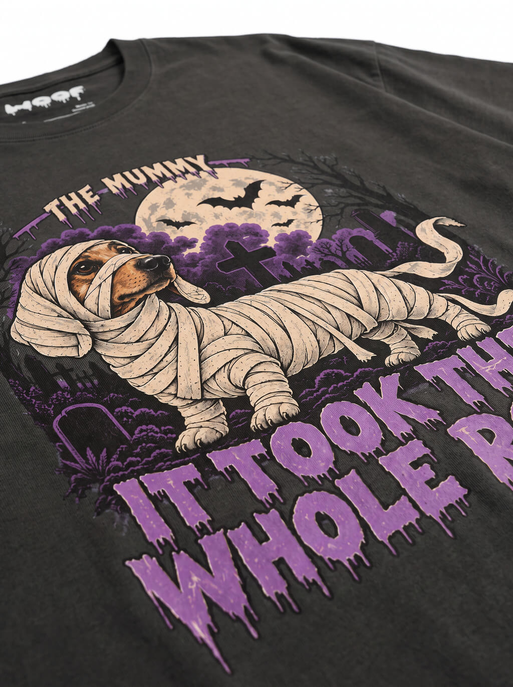 Close-up of the "It Took the Whole Roll" print with a mummy-wrapped Dachshund on the Washed Black tee