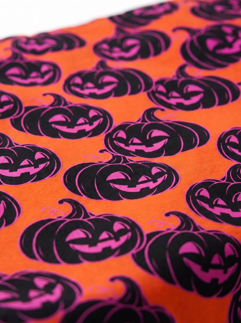 Close-up of the black and pink jack-o-lantern pattern on the orange Halloween dog bandana