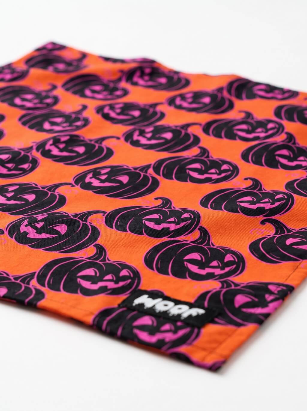 Orange Halloween dog bandana angled, showing the pumpkin pattern and the woven WOOF label