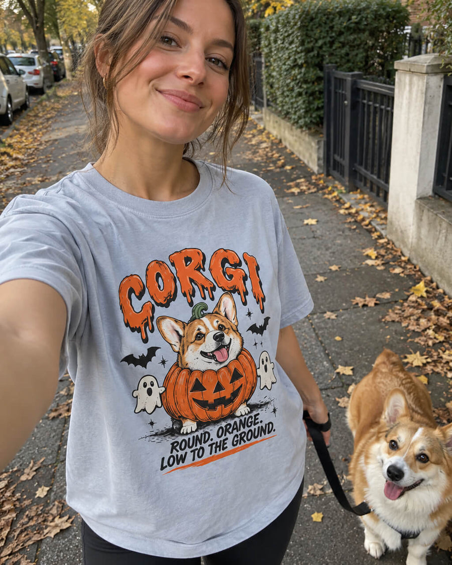 Pumpkin Patch Corgi oversized Halloween T-shirt in Light Washed Denim worn by a woman walking her Corgi on a leash along an autumn sidewalk