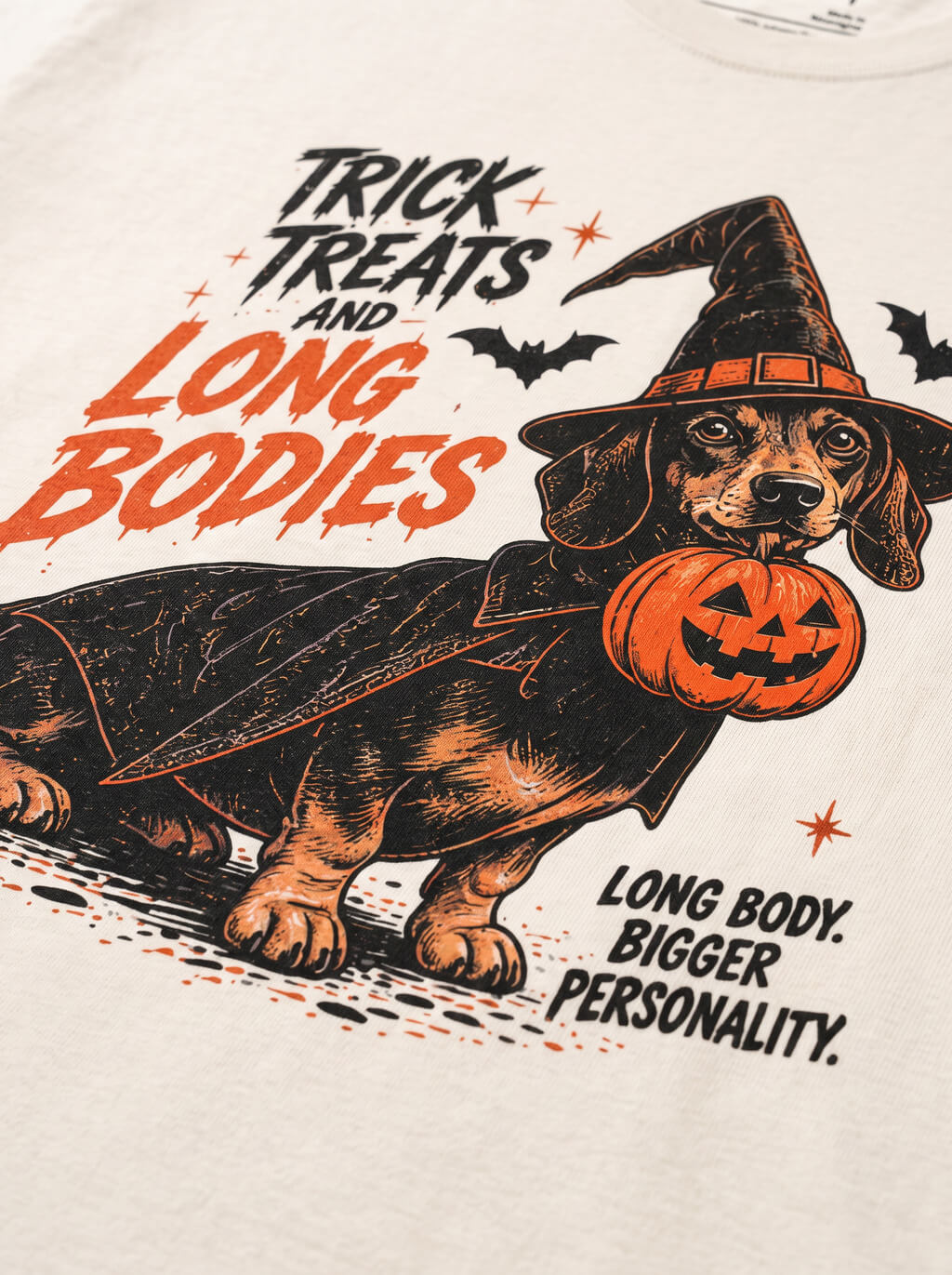 Close-up of the "Trick, Treats & Long Bodies" print with a Dachshund in a witch hat with a pumpkin bucket on the Vintage White tee